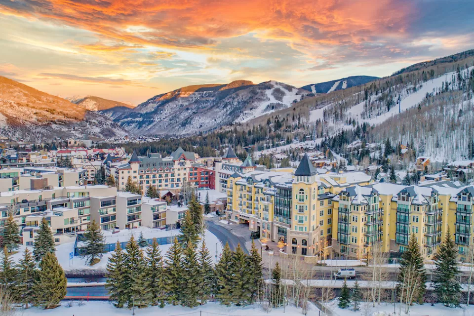 Aerial view of Vail, Colorado in winter with multi-story buildings in foregorund and snowy mountains in background.